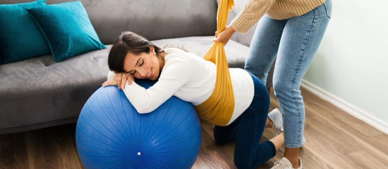 Pregnant woman relaxing while a midwife wraps a rebozo in her belly